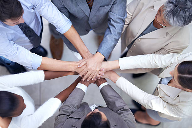 A diverse group of people standing together, holding hands, and forming a circle, symbolizing collaboration and unity for sustainable innovation. They are surrounded by lush greenery and sustainable infrastructure, portraying the concept of sustainable cities and a harmonious relationship with nature.